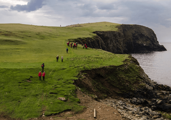 Wir wandern auf Fair Isle über grüne Wiesen entlang der Küste zu den Vogelbrutstätten.